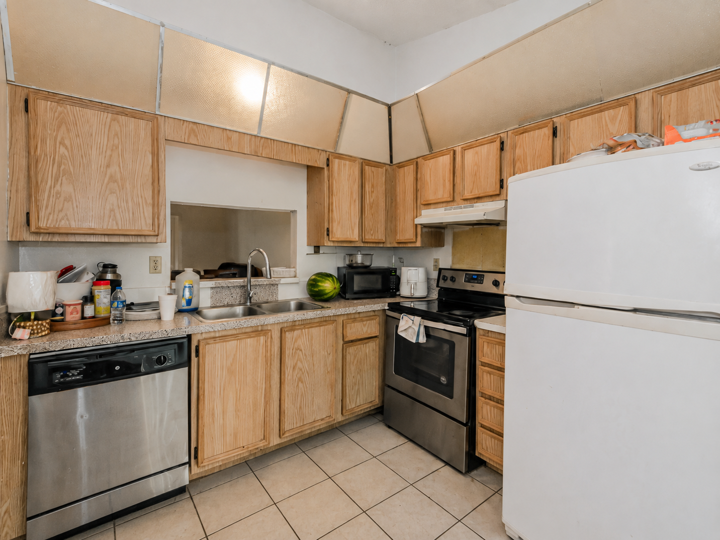 Cluttered kitchen with bottles, dishes and groceries crowding the counters